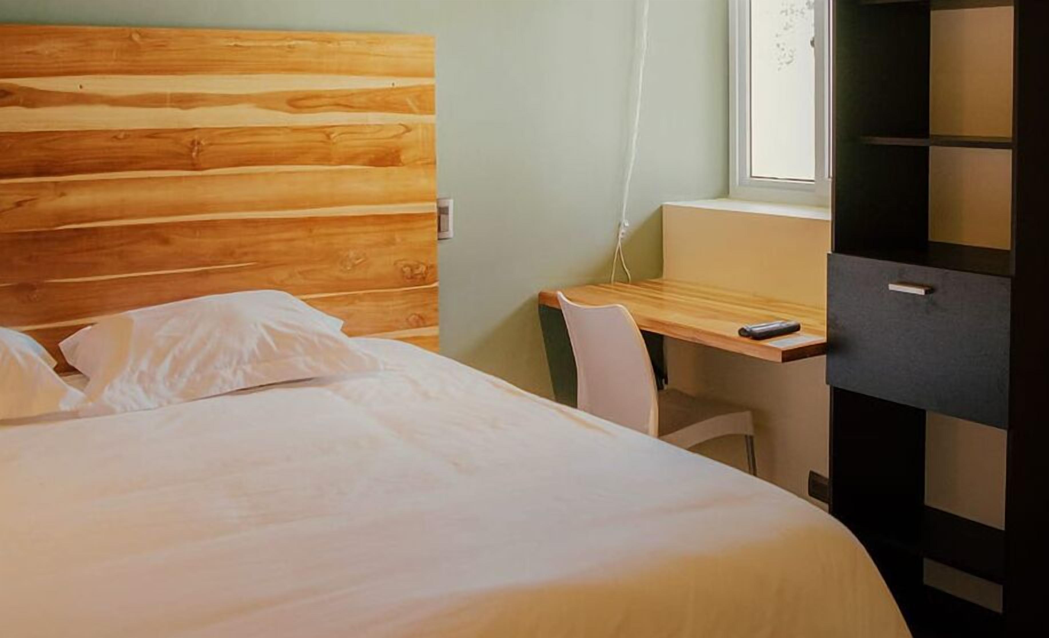 Une chambre à coucher avec une tête de lit en bois, un lit avec une literie blanche, un bureau avec une chaise et une armoire.