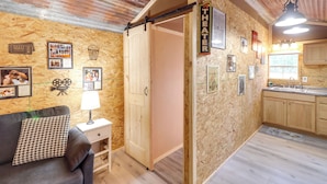 Ett mysigt rum med en soffa, ett litet bord med en lampa, en trädörr och en köksdel med träskåp och ett handfat.