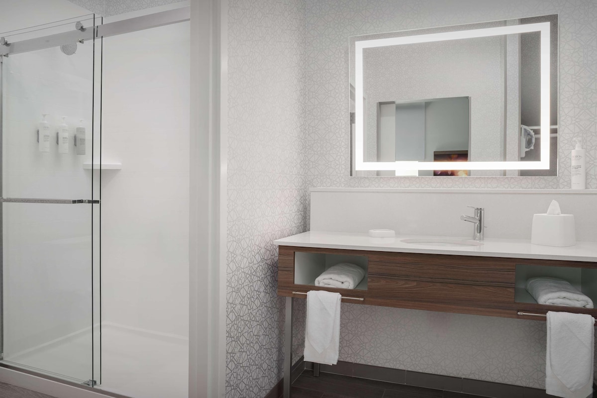 A modern bathroom with a glass shower enclosure, a wooden vanity with a mirror, and a towel rack.