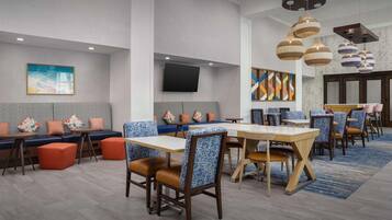 A modern dining area with booths and tables, a flat-screen TV, and decorative wall art.