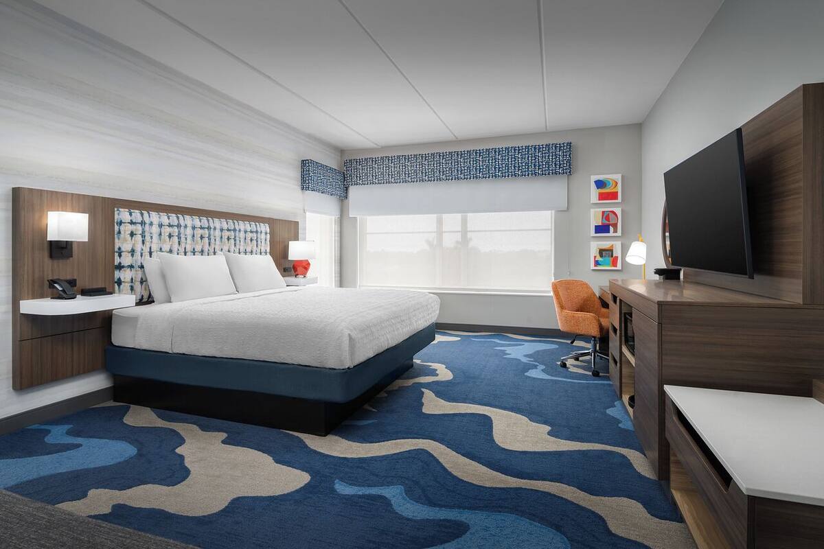 A hotel room with a bed, a desk, a TV, and a window.