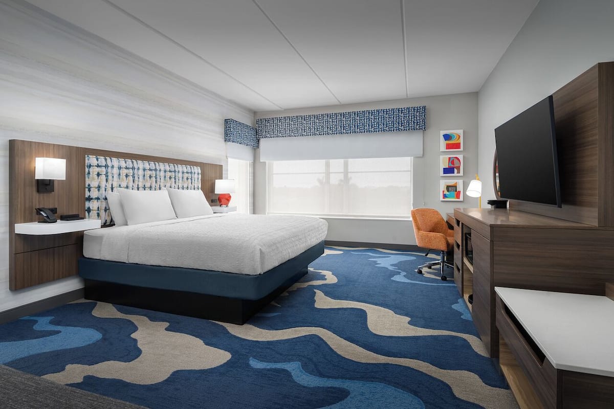A hotel room with a bed, a desk, a TV, and a window.
