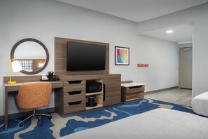 Ein Hotelzimmer mit einem großen Flachbildfernseher, einem Holzbüro, einem Stuhl, einer Mikrowelle, einer Kaffeemaschine und einem blauen Teppich mit Muster.