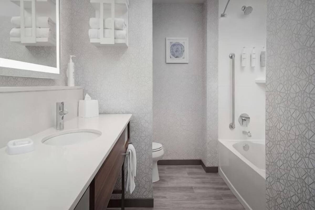 A modern bathroom with a large mirror, two sinks, a toilet, and a bathtub.