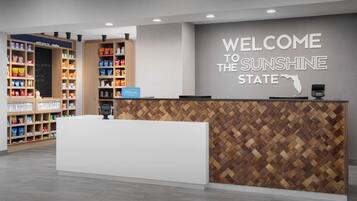 A hotel reception desk with a welcome sign, snack shelves, and a payment terminal.