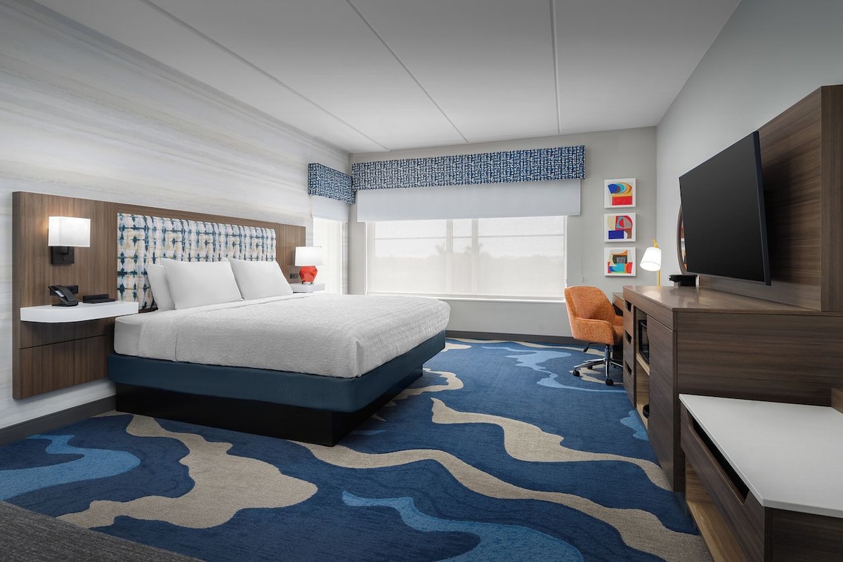 A hotel room with a bed, a desk, a TV, and a window.