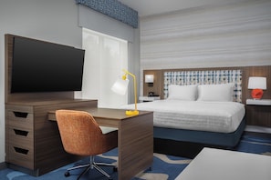 A hotel room with a wooden desk, a television, a chair, a bed with white bedding, and a nightstand with a lamp. - Hampton Inn And Suites By Hilton Naples South (Naples)