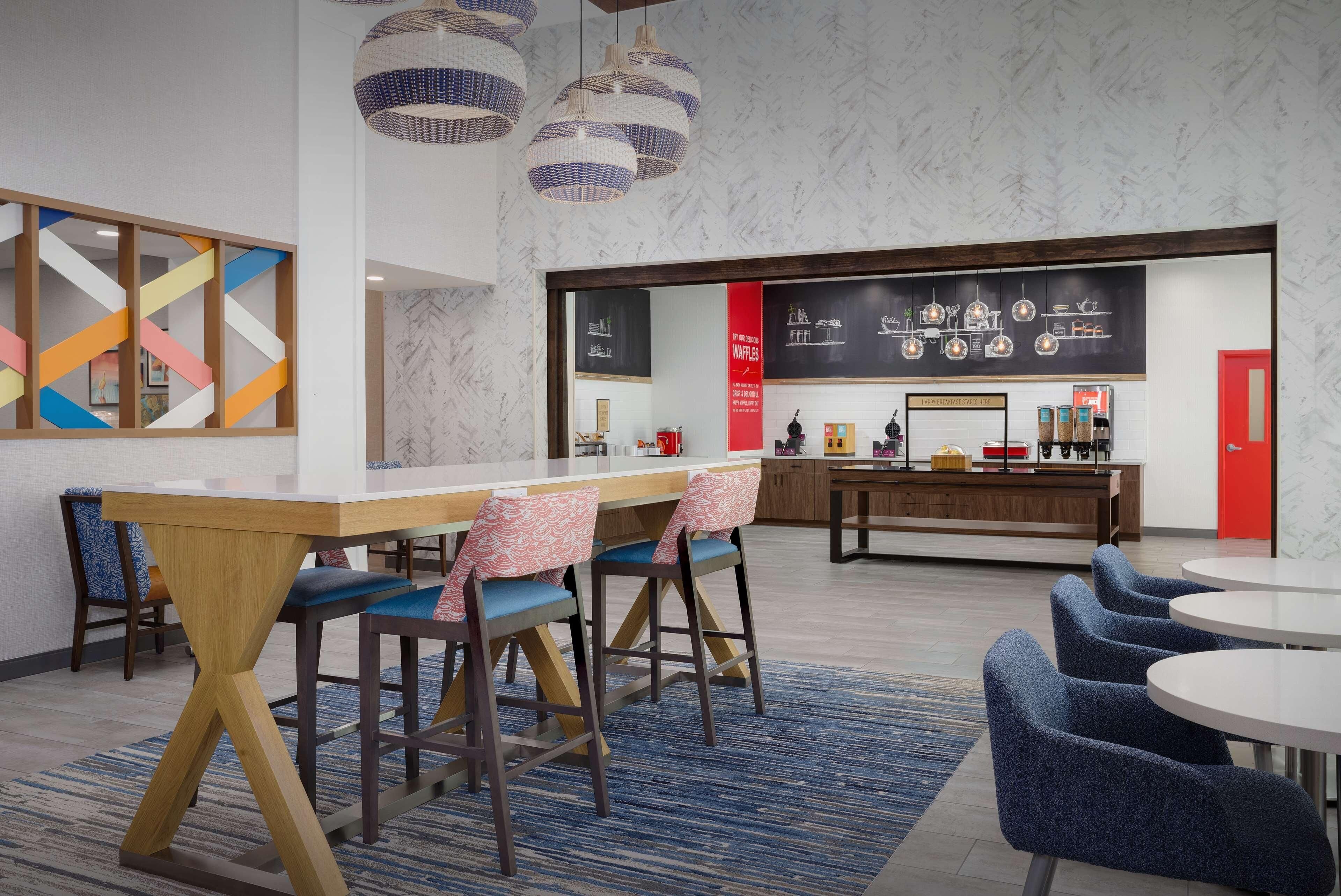 A modern dining area with a wooden table, blue chairs, and hanging pendant lights.