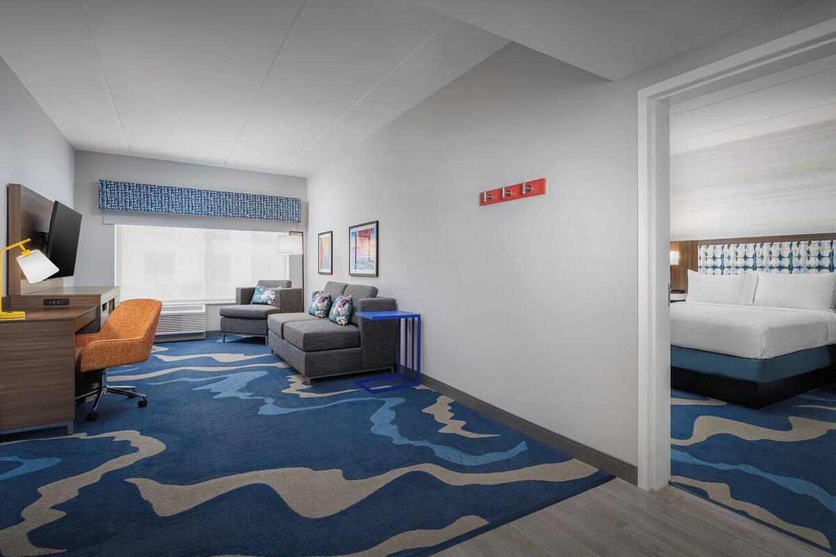 A hotel room with a desk, chair, sofa, and bed.