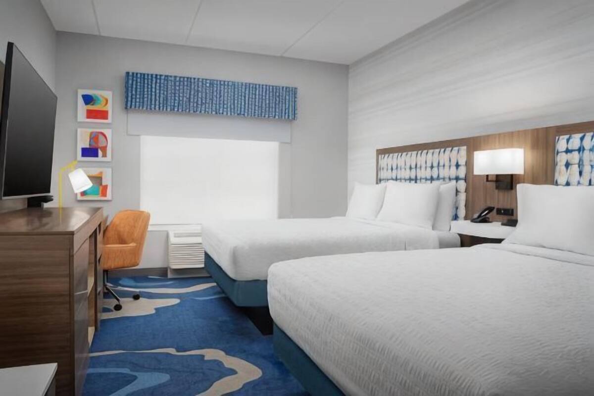 A hotel room with two beds, a desk, a chair, a television, and a window.