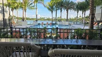 A poolside view with a glass of white wine, palm trees, and lounge chairs.