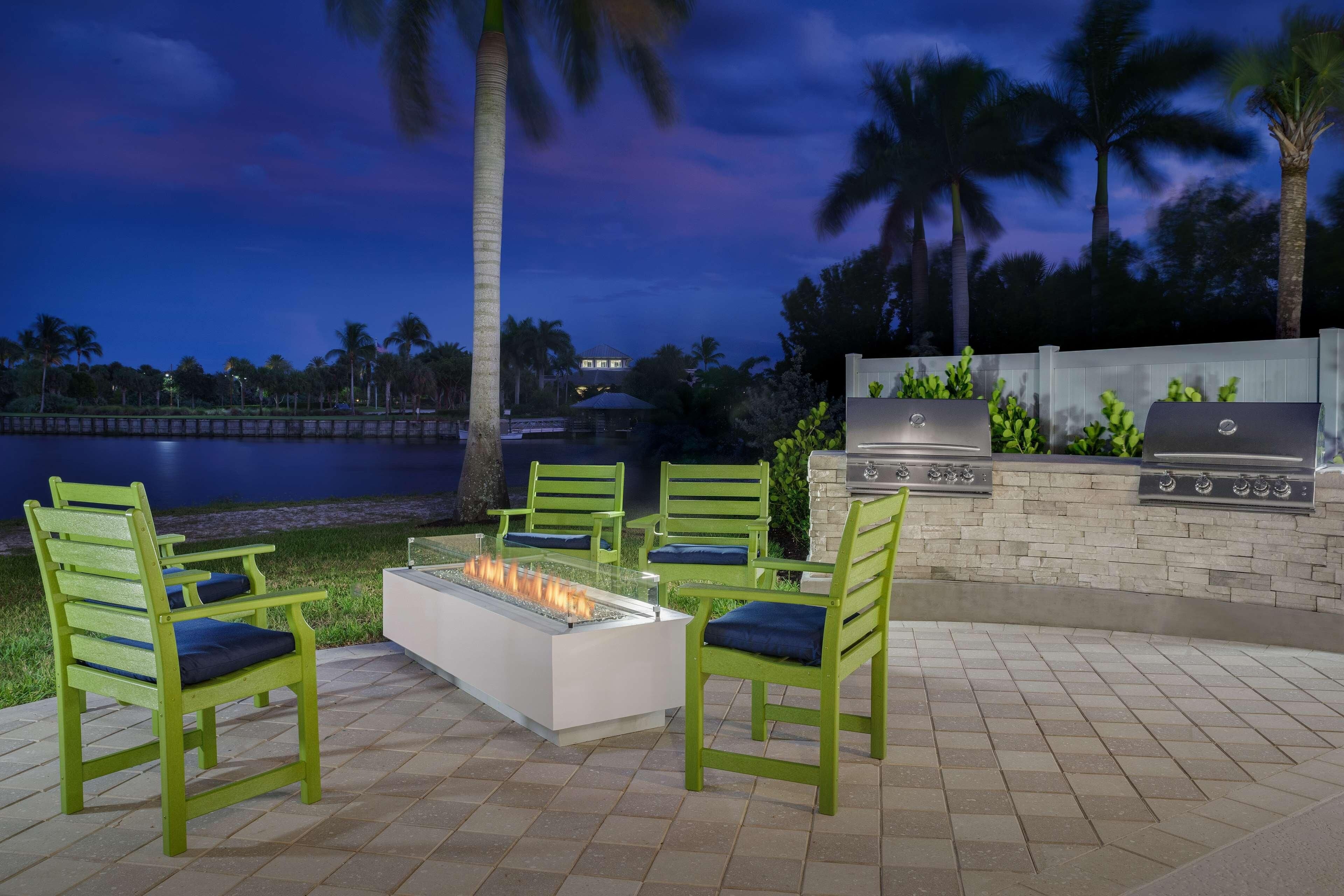 An outdoor patio with green chairs, a fire pit, and a barbecue grill.