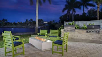 An outdoor patio with green chairs, a fire pit, and a barbecue grill.