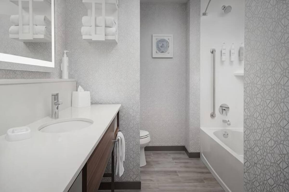 A modern bathroom with a large mirror, two sinks, a toilet, and a shower area.