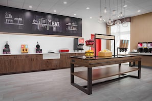 A modern breakfast area with a chalkboard menu, coffee machines, and a red sign indicating breakfast is served. - Hampton Inn And Suites By Hilton Naples South (Naples)