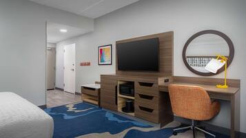 A hotel room with a bed, a desk with a chair, a television, a microwave, and a large mirror.