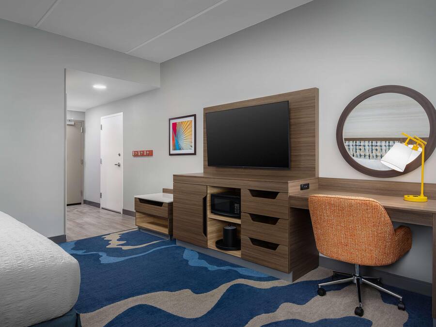 A hotel room with a bed, a desk with a chair, a television, a microwave, and a large mirror.