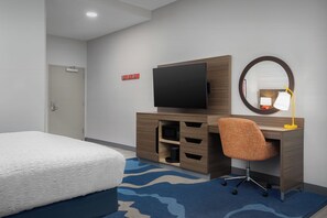 A hotel room with a bed, a desk with a chair, a television, a mirror, and a small lamp. - Hampton Inn And Suites By Hilton Naples South (Naples)