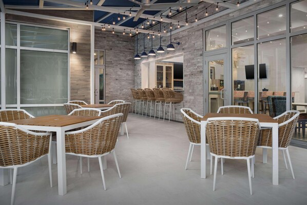 A modern dining area with wicker furniture, a glass wall, and a ceiling fan. - Hampton Inn And Suites By Hilton Naples South (Naples)