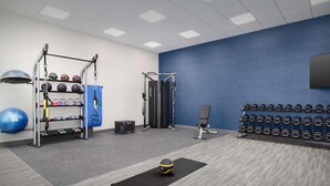Un gimnasio con equipo de ejercicio, un televisor montado en la pared y una hilera de mancuernas.