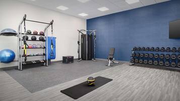 A gym with exercise equipment, a wall-mounted TV, and a row of dumbbells.