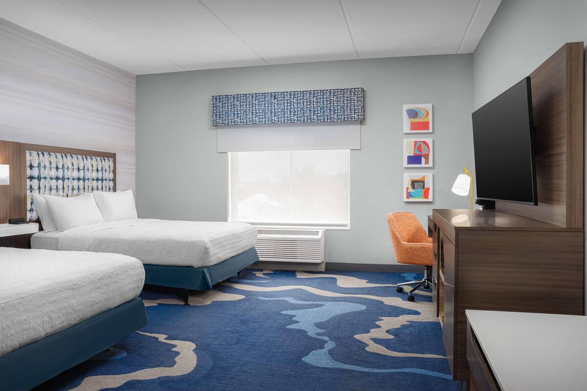 A hotel room with two beds, a desk, a TV, and a window with a view.