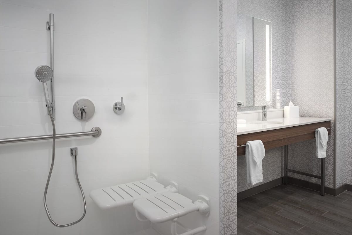 A modern bathroom with a walk-in shower, a toilet with a grab bar, a sink with a mirror, and a towel rack.