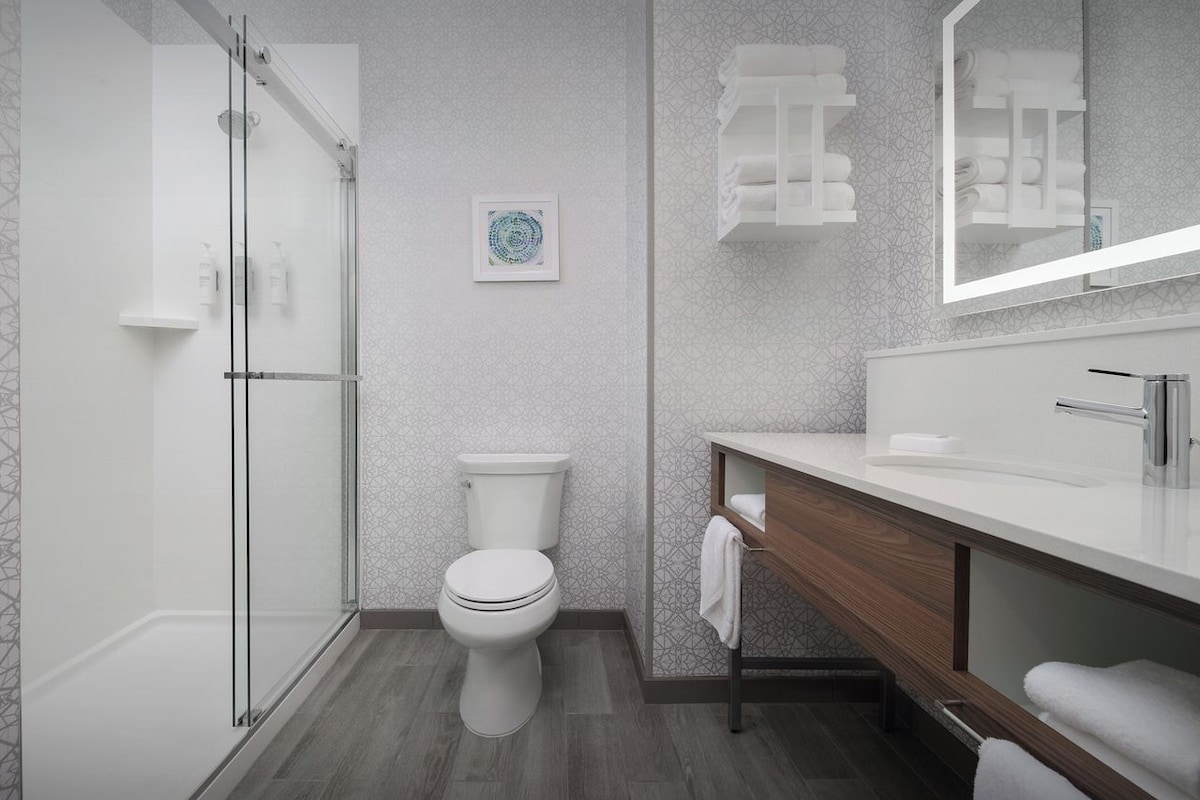 A modern bathroom with a glass-enclosed shower, a white toilet, and a wooden vanity with a mirror.