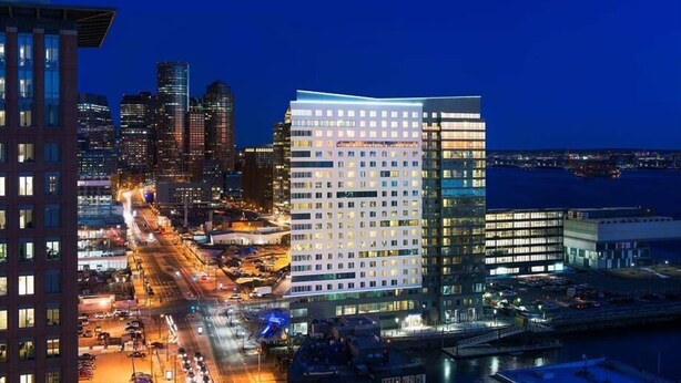 A modern hotel with a prominent glass facade, situated in a bustling urban area with a view of the waterfront. - Boston Harbor 1 BR | Desk+Wi-Fi | Kitchen (Boston)