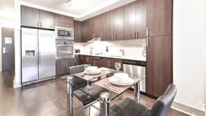 A modern kitchen with stainless steel appliances, dark wood cabinets, and a glass dining table set for four. - Boston Harbor 1 BR | Desk+Wi-Fi | Kitchen (Boston)