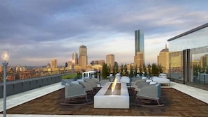 A rooftop lounge with a long table and chairs, overlooking a city skyline with modern buildings. - close to subway 1 BR | near Restaurant Row (Boston)