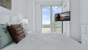 Une chambre d’hôtel moderne dotée d’un grand lit, d’un téléviseur fixé au mur et offrant une vue sur le paysage urbain grâce à une grande fenêtre.