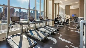 Une salle de sport équipée de tapis de course, de vélos d’exercice et offrant une vue sur la ville.