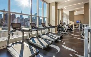 A gym with treadmills, exercise bikes, and a city view.