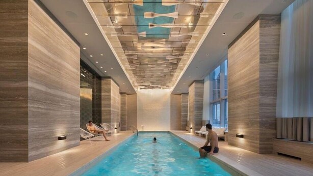 Una piscina interior con diseño moderno, que cuenta con una fuente central y zonas de estar a lo largo de los bordes.
