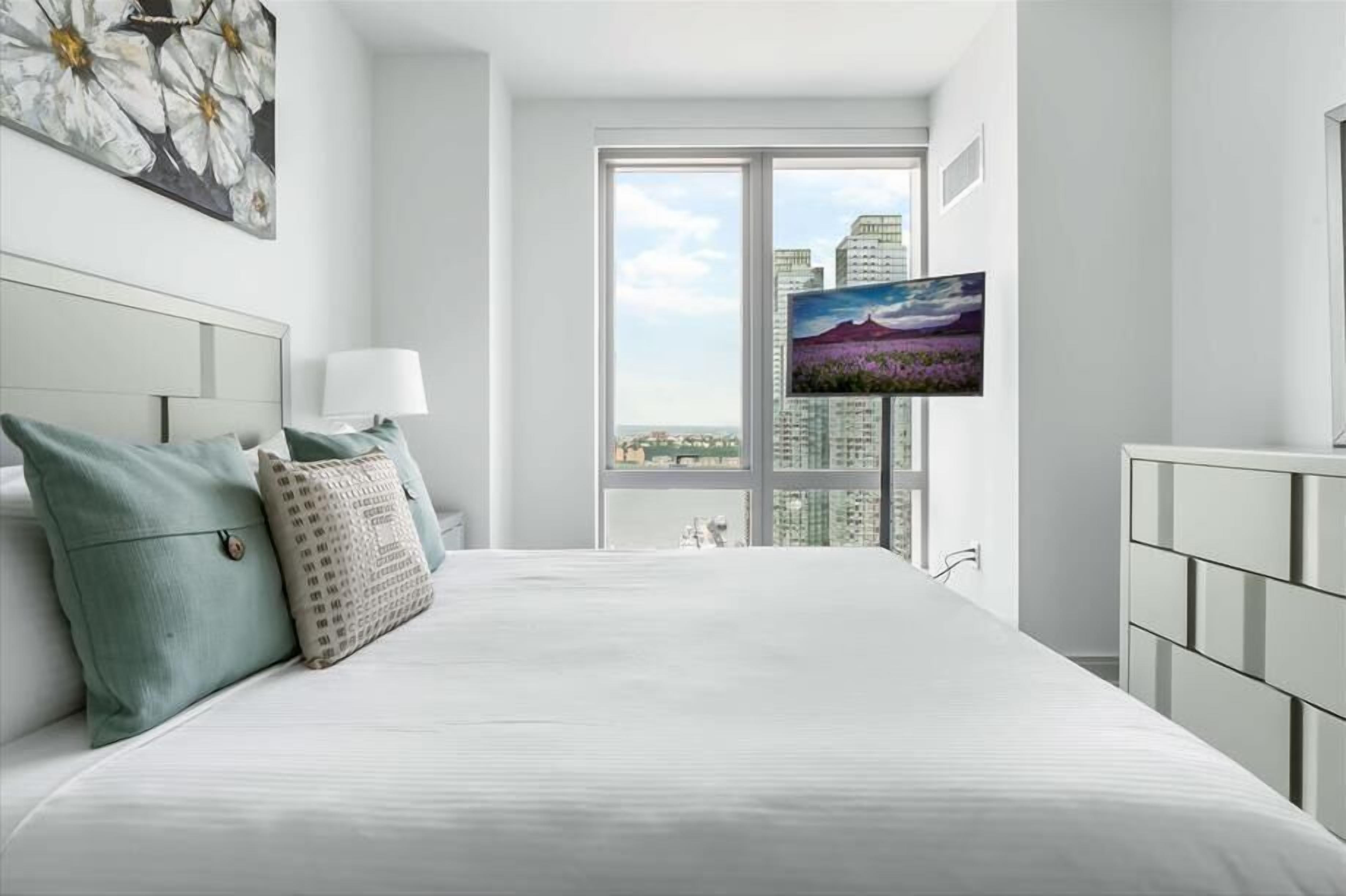 Ein modernes Hotelzimmer mit einem großen Bett, einem an der Wand befestigten Fernseher und Blick auf die Stadt durch das Fenster.