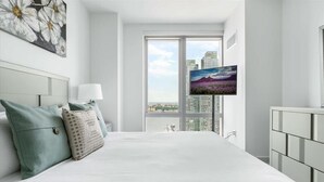 Ein modernes Hotelzimmer mit einem großen Bett, einem an der Wand befestigten Fernseher und Blick auf die Stadt durch das Fenster.