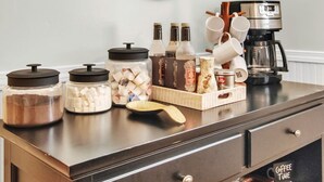 A kitchen counter with jars of sugar, coffee, and tea, a coffee maker, and a mirror on the wall.