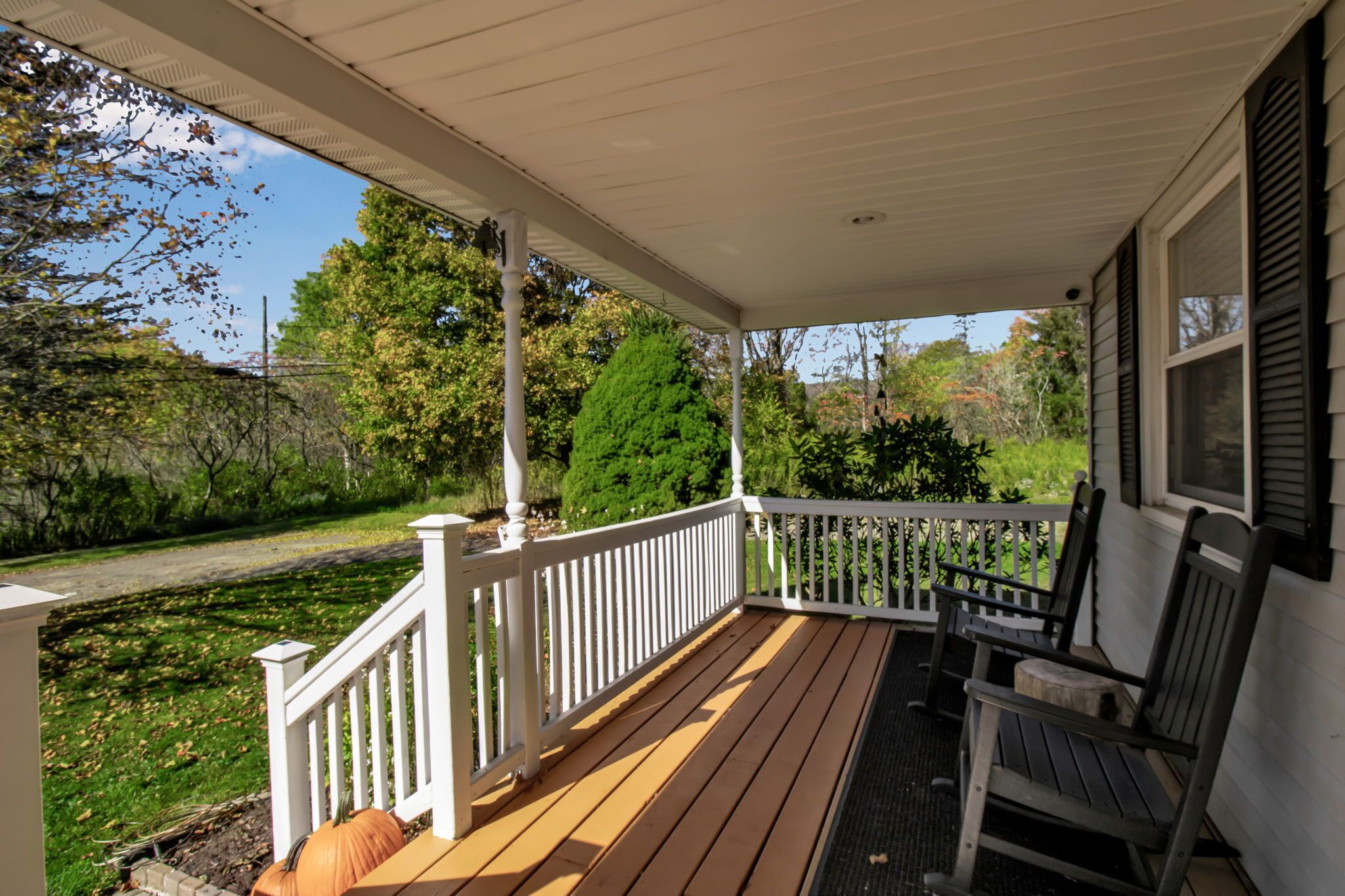 A covered porch with a wooden deck, white railings, and two wooden chairs.