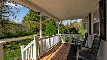 A covered porch with a wooden deck, white railings, and two wooden chairs.