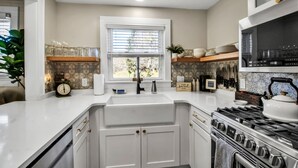 A modern kitchen with white cabinetry, a stainless steel stove, and a window with blinds.