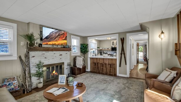 A spacious living room with a fireplace, a television mounted above it, and a kitchen in the background.