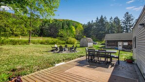 A wooden deck with outdoor furniture, a small shed, and a house in a lush green setting.