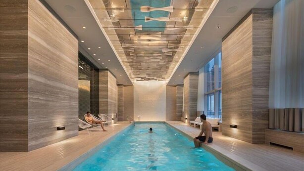 Una piscina interior moderna con agua azul cristalina, rodeada de paredes de madera y amplias ventanas.