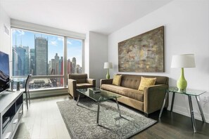 A modern living room with a city view, a sofa, two armchairs, a glass coffee table, and a painting on the wall.