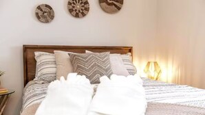 Un lit bien fait, agrémenté de coussins à motifs et d’une couverture, une lampe de chevet et trois éléments décoratifs fixés au mur.