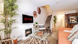 Un salon avec une cheminée, une table basse en verre, un canapé et un téléviseur affichant le logo « NETFLIX ».
