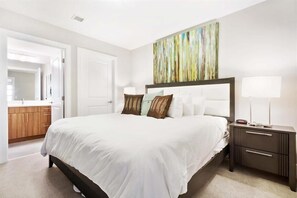 A hotel room with a large bed, a nightstand with a lamp, and a painting on the wall. - Steps to Metro 2 BR | Pentagon City | Pet-Friendly (Arlington)