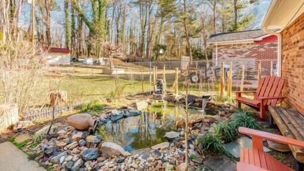 A backyard with a pond, a wooden deck, and a red chair. - Midcentury Charm by the Pond (Winston-Salem)