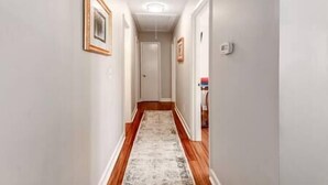 A narrow hallway with wooden flooring and a patterned rug. - Midcentury Charm by the Pond (Winston-Salem)